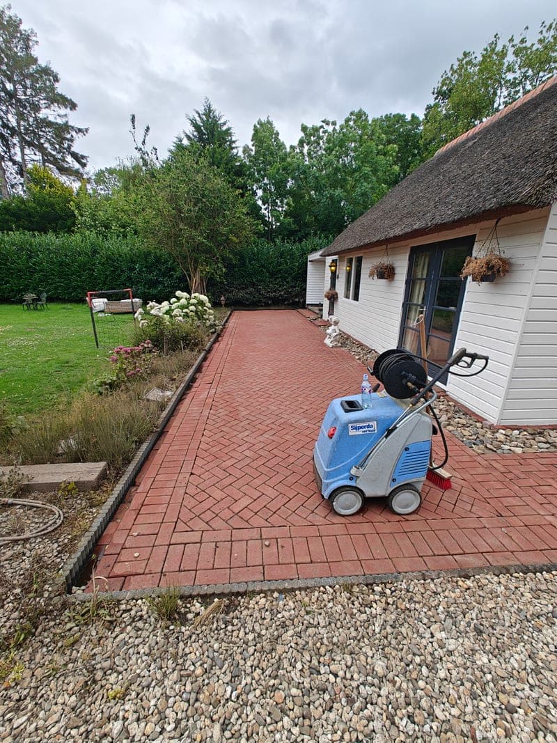 De hogedrukreiniger op een pas gereinigd terras van rode klinkers